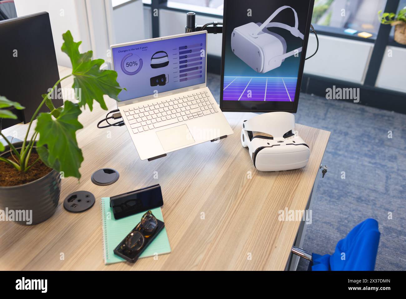 Desk with laptop displaying graphs and VR tech in contemporary business office Stock Photo