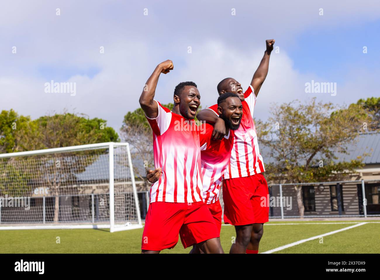 Three African American young male athletes celebrate on soccer field Stock Photo