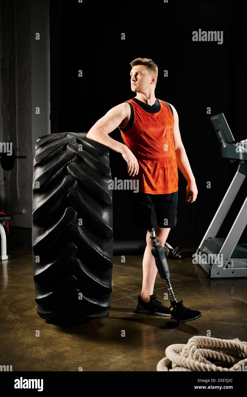 A disabled man with a prosthetic leg stands proudly next to a large tire in a gym, showcasing