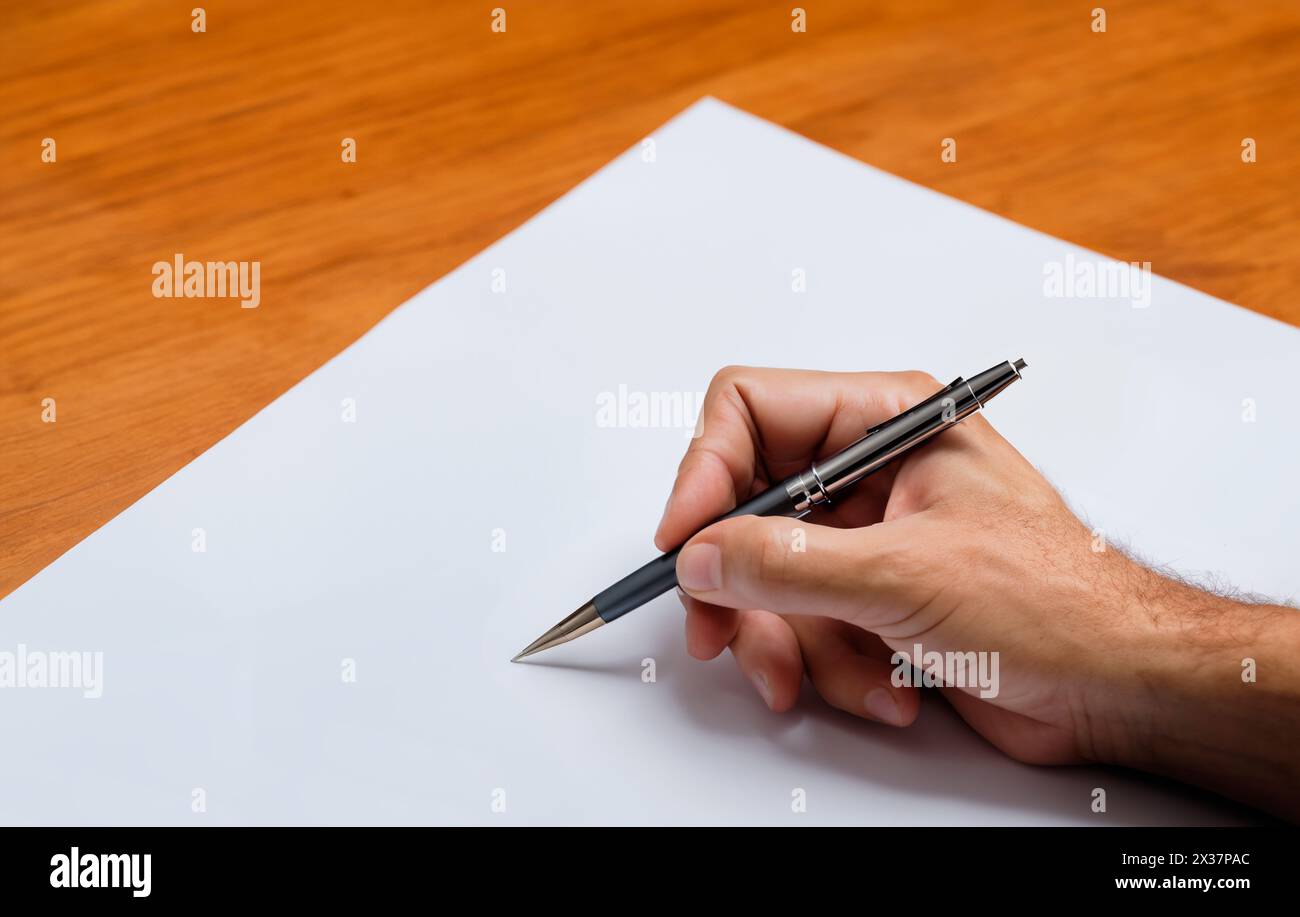 Man starts writing holding a ballpoint on a blank sheet of paper. Hand is ready for writing. Writer's block Stock Photo