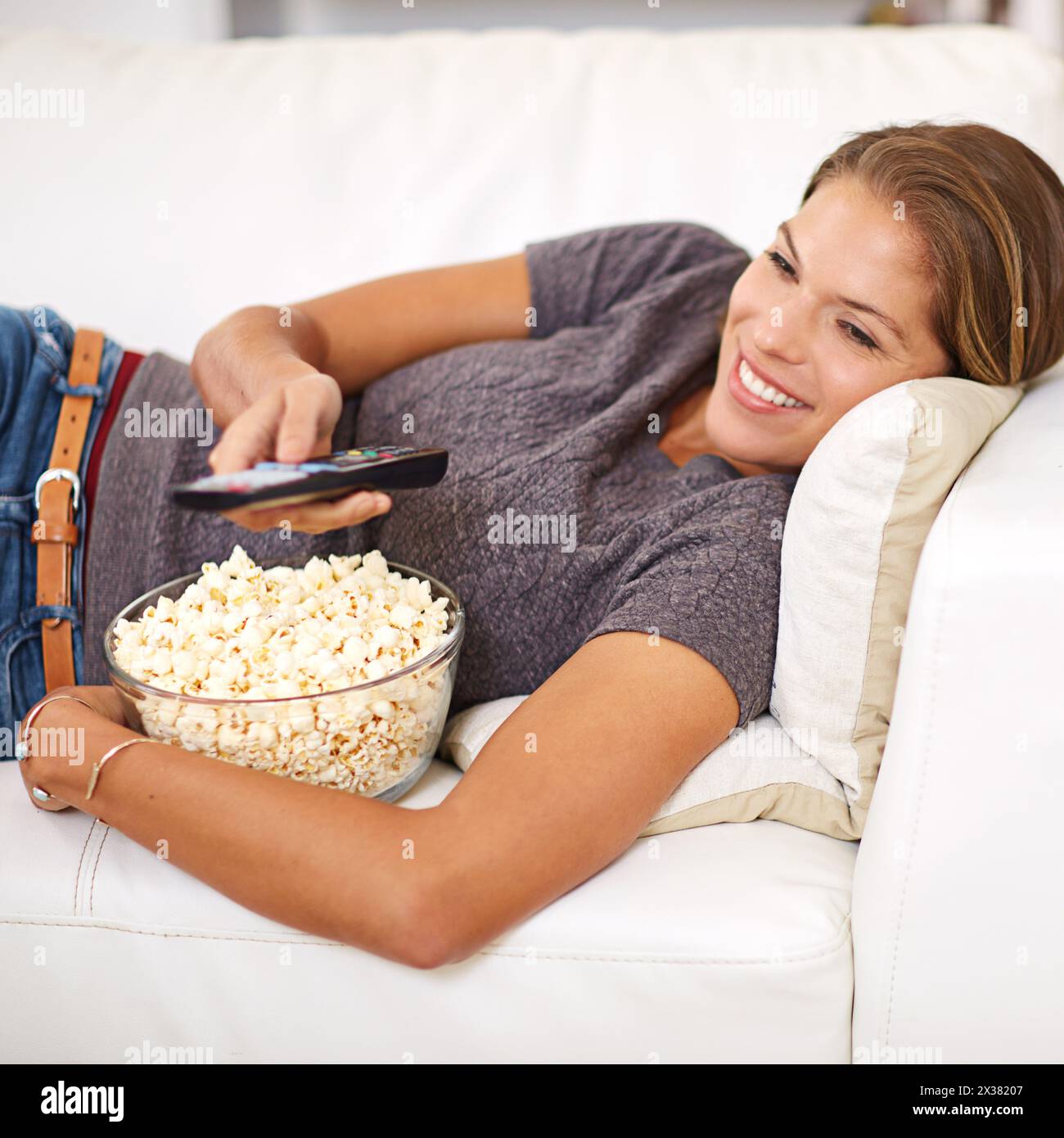 Woman, sofa and food with remote and relax in home, popcorn and watching on weekend. Holiday, entertainment and break with movie or show, streaming or Stock Photo