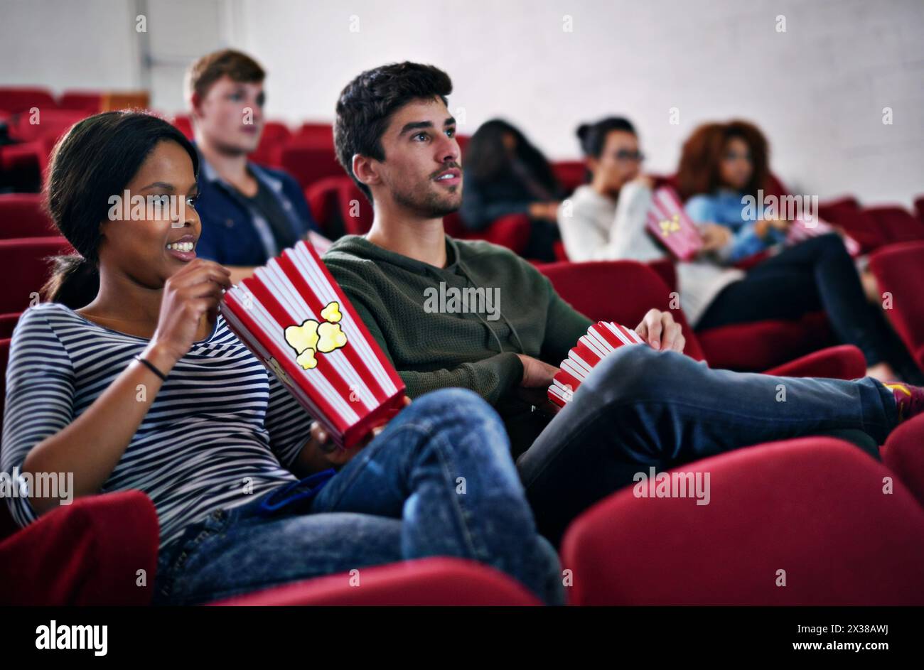 Movie, date and couple in cinema at night with popcorn to relax and watch in theatre with happiness. Film, experience and people in audience enjoy Stock Photo