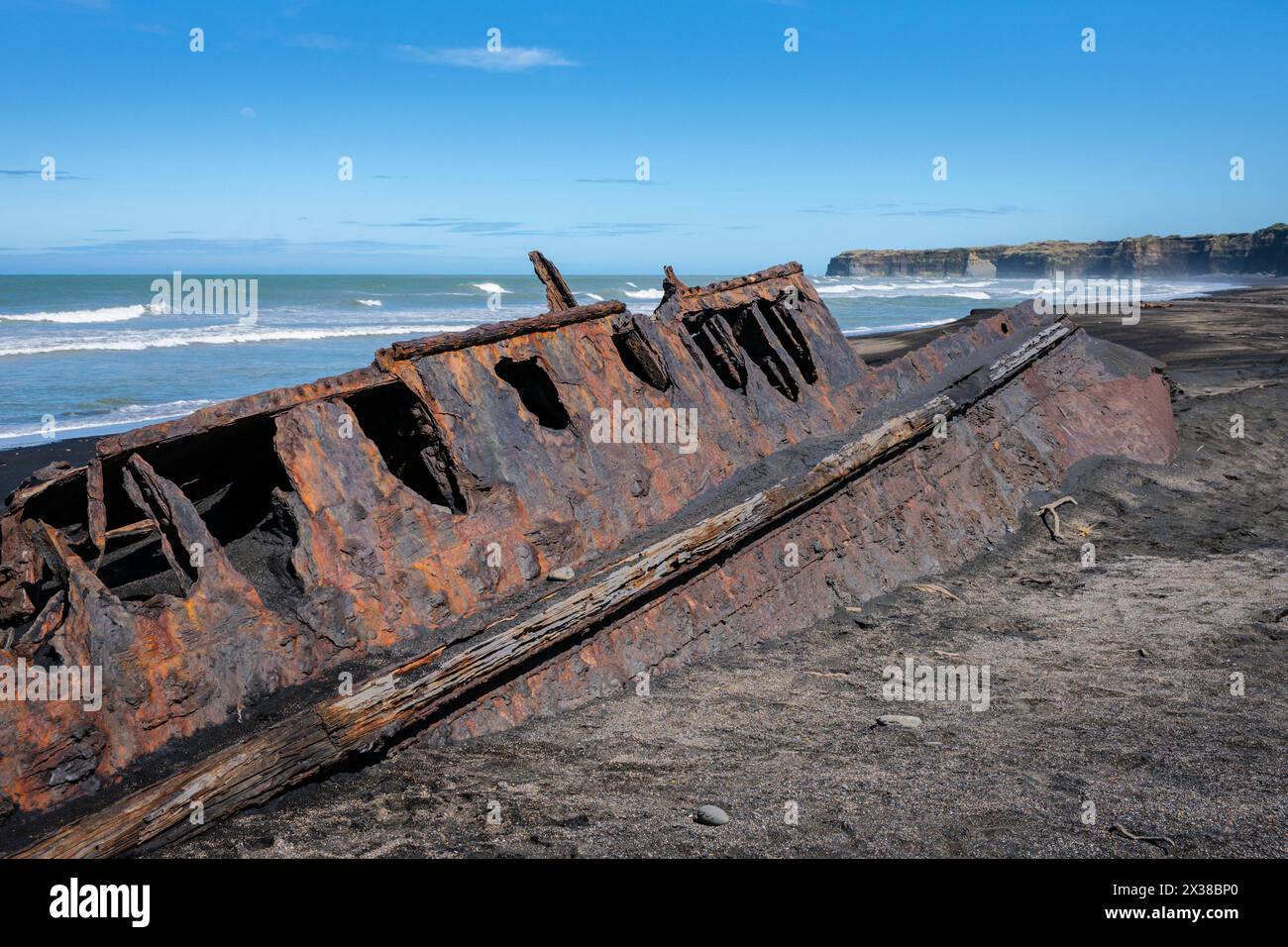 The rusting hulk of a boat half-buried in the black sand of Patea Beach, Taranaki, North Island, New Zealand Stock Photo