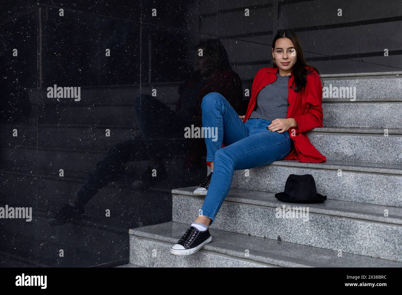 Portrait of young Latin American woman sitting on stairs. Poses with ...