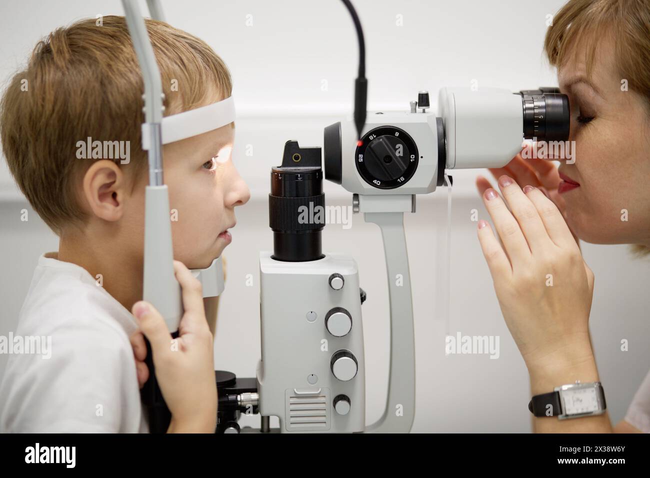 Female doctor examines eyes of boy through slit lamp. Stock Photo