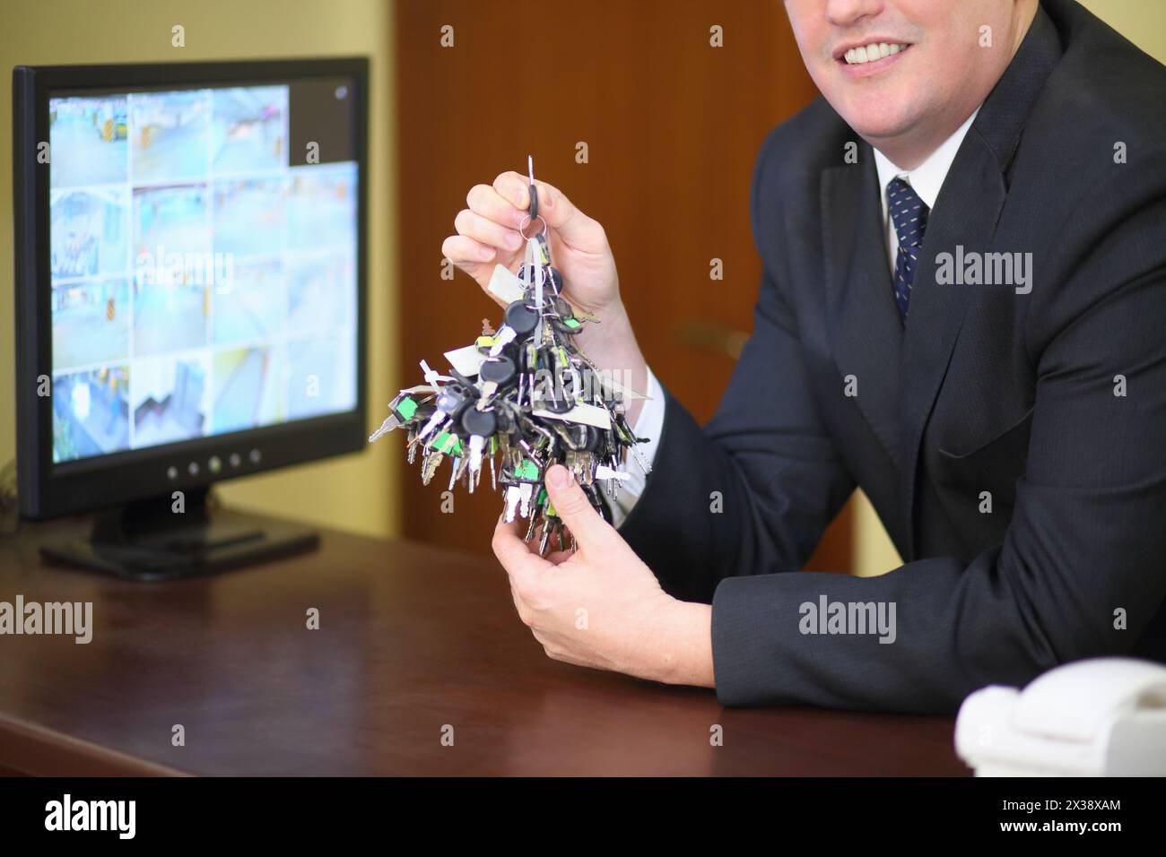 A large bunch of keys in the hands of a smiling concierge near the monitor with CCTV Stock Photo