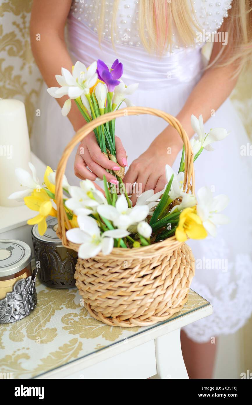 Woman in white dress takes flower from basket on table in studio, noface Stock Photo