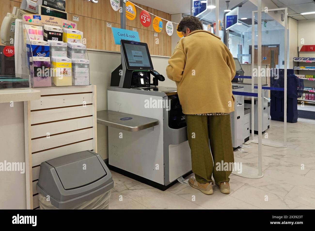 Boots The Chemist shop interior back view of model released pensioner woman perplexed by new instore automated payment till & screen Essex England UK Stock Photo