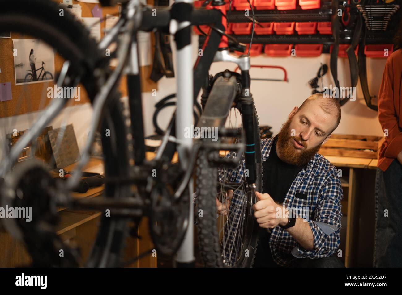 Bike service, repair and upgrade concept. Cycling mechanic fixing bicycle wheel in workshop. Bike repairman. Stock Photo