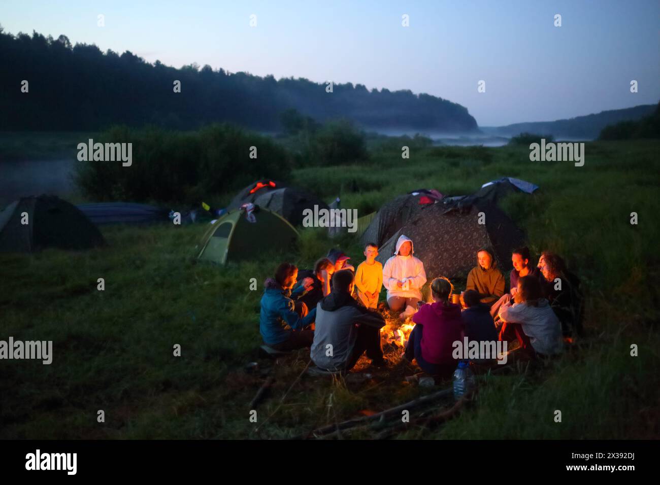 TVER REGION, RUSSIA - JUL 3, 2016: Tourists sits near fire near river. Tvertsa - river in Tver region of Russia. Length - 188 km. The river is used by Stock Photo
