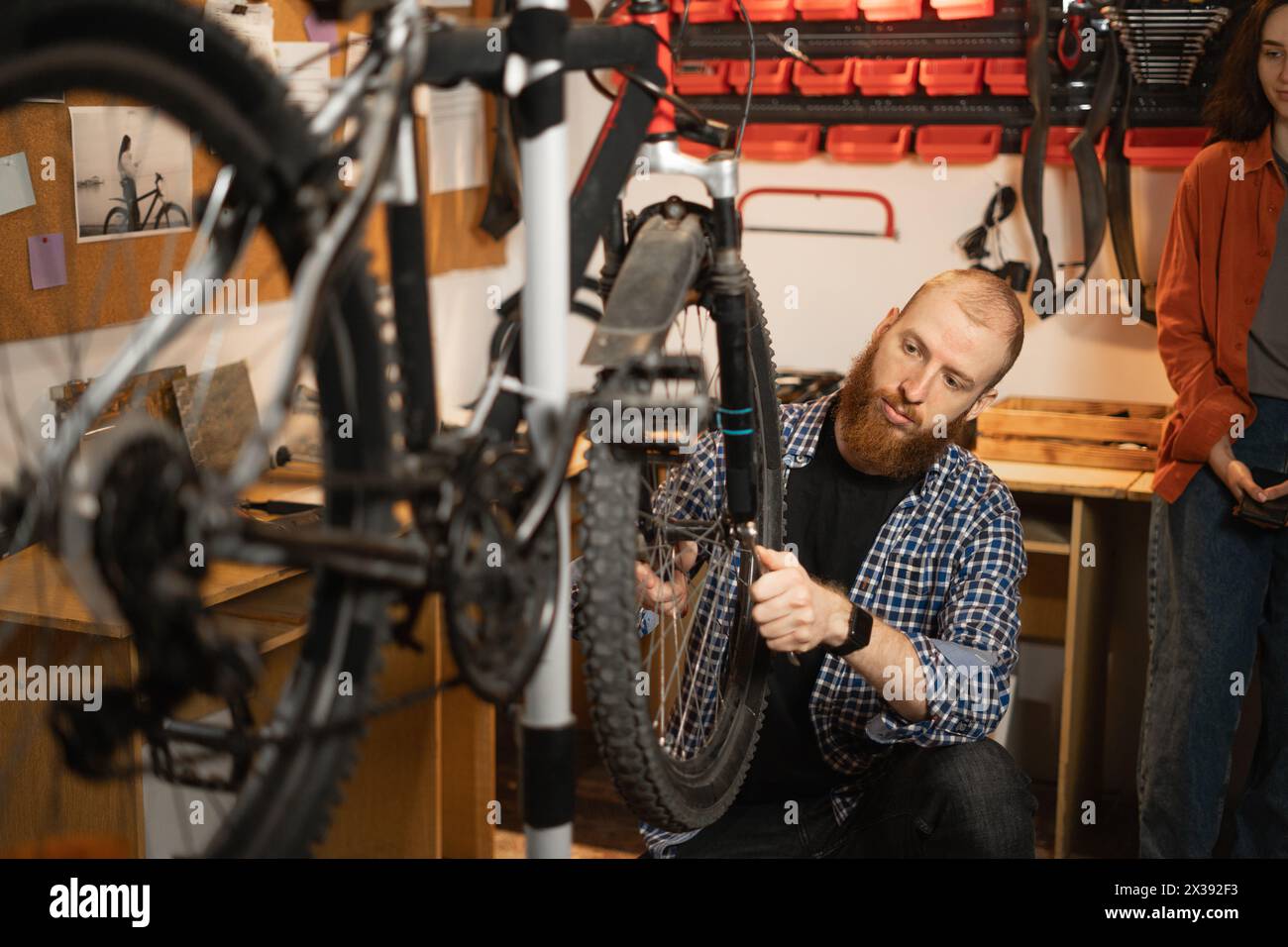 Bike service, repair and upgrade concept. Two cycling repairman fixing wheels on bicycle in workshop. Young girl and man working in garage. Stock Photo