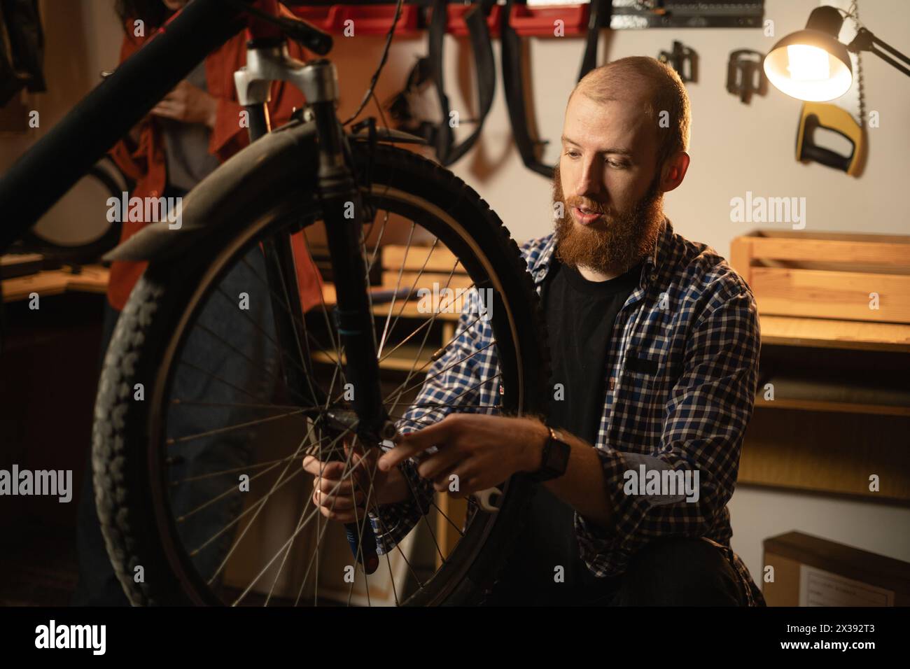 Cycling mechanic checking bicycle wheel spoke, fixing bicycle in workshop. Bike service, repair and upgrade Stock Photo