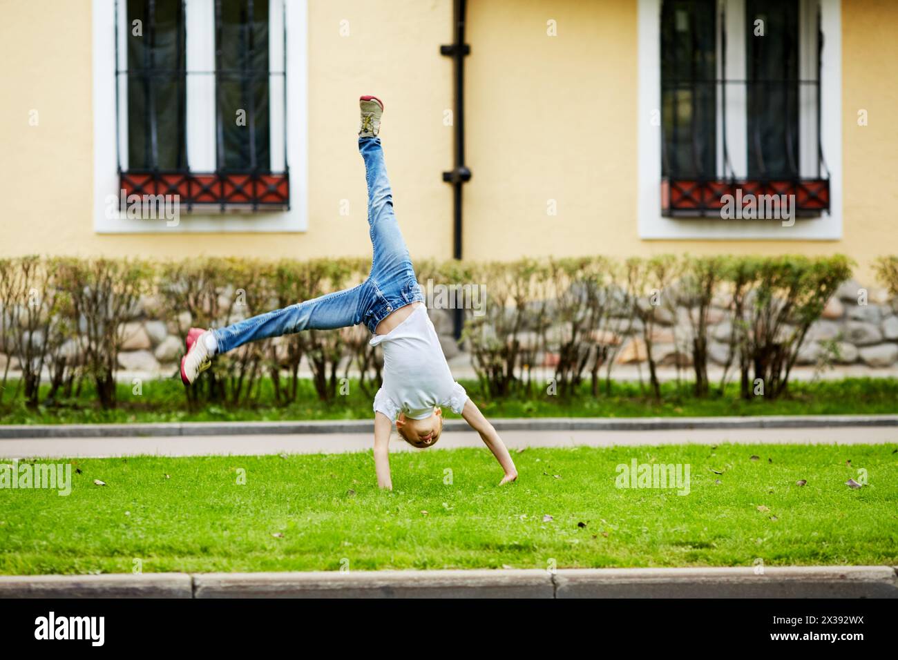 Girl turns cartwheel on grassy lawn in front of house. Stock Photo
