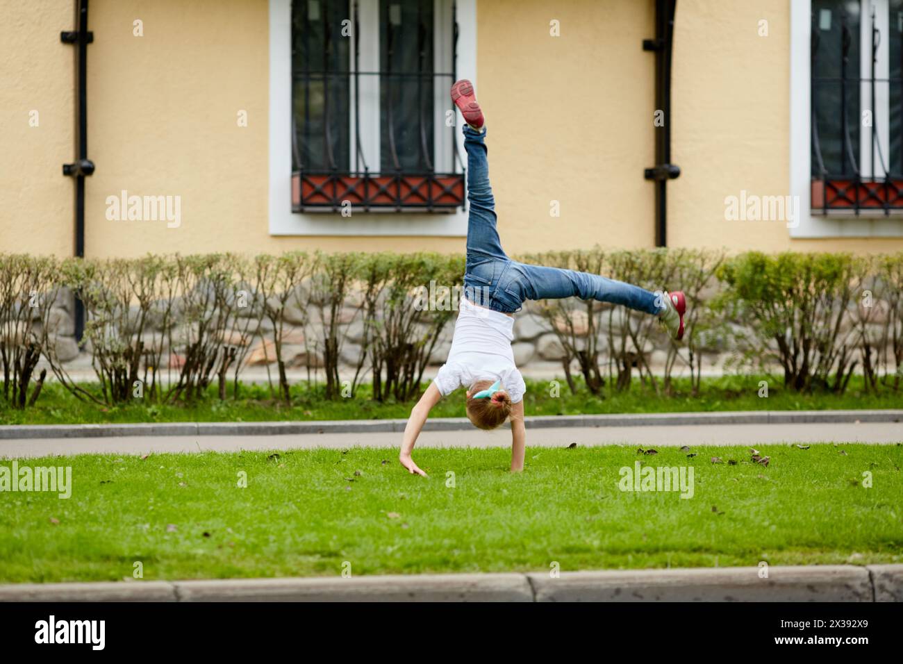 Girl turns cartwheel on grassy lawn in front of house. Stock Photo