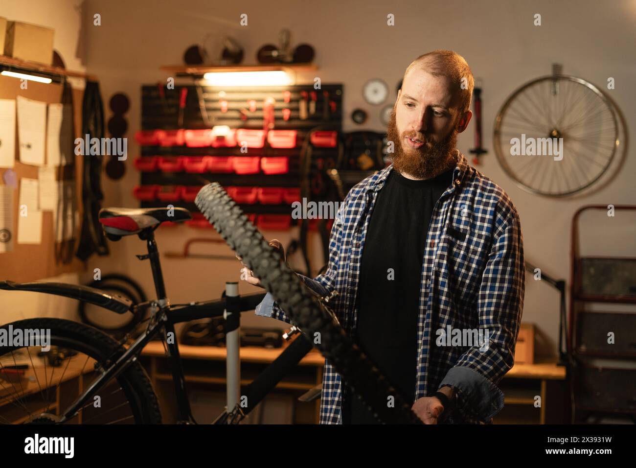 male bearded worker holding and repairing bicycle wheel while standing in bicycle workshop or authentic garage Stock Photo