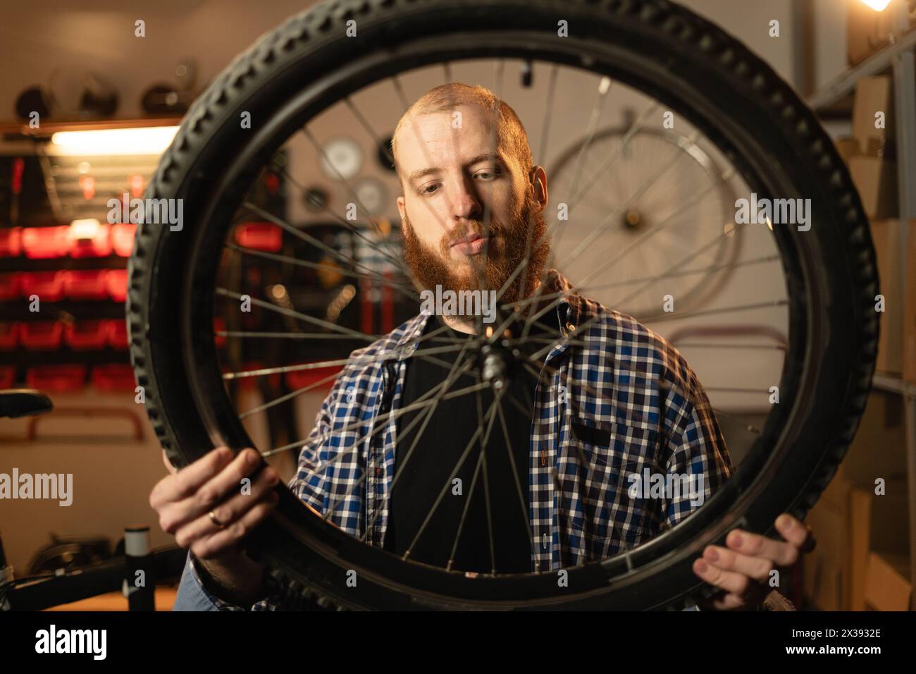 Bearded man standing alone in his workshop or garage and repairing a bicycle wheel. Stock Photo