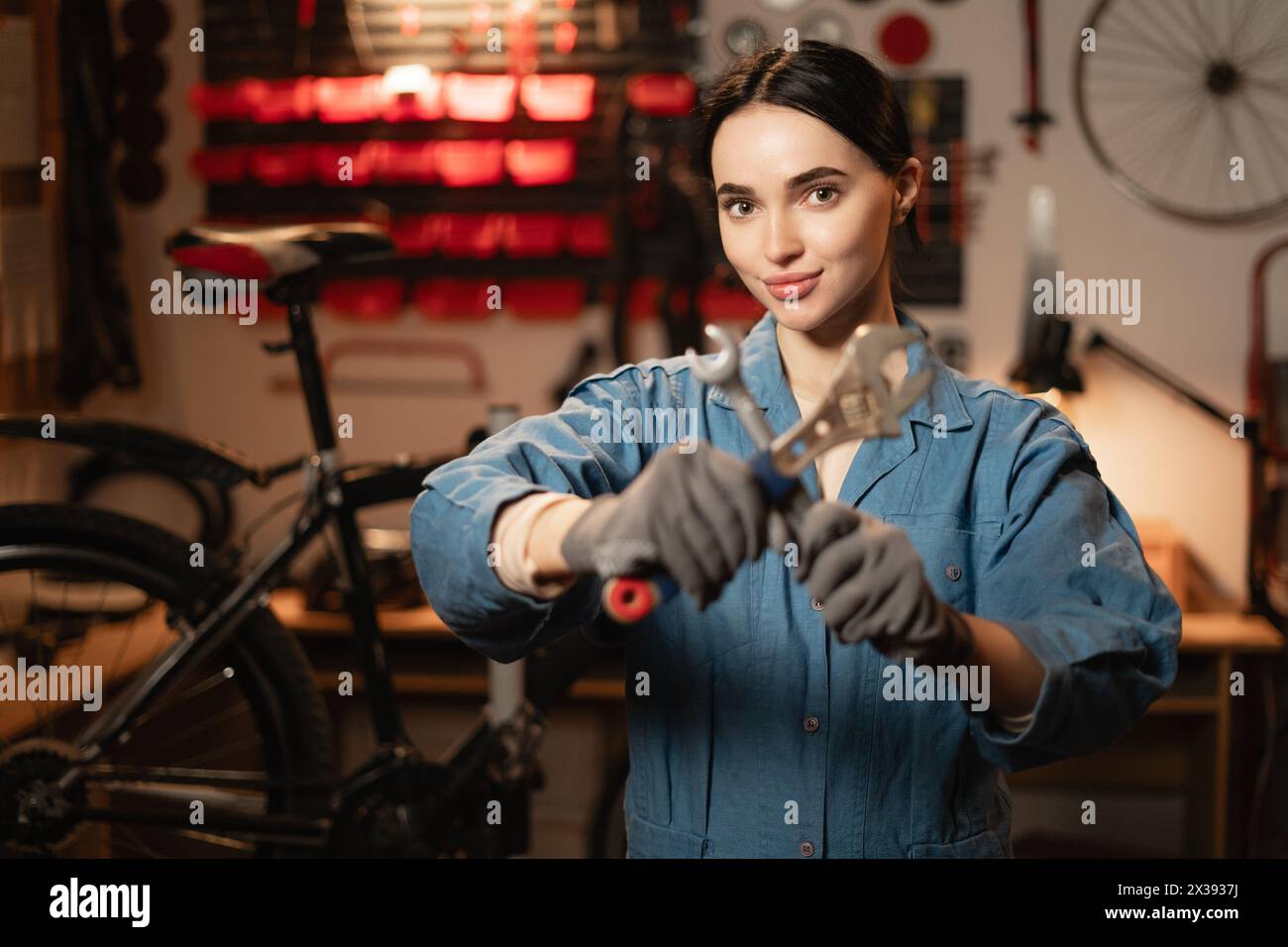 Bicycle care maintenance and servicing concept. Portrait of female technician mechanic using the wrench to repairing bike service support in garage or Stock Photo