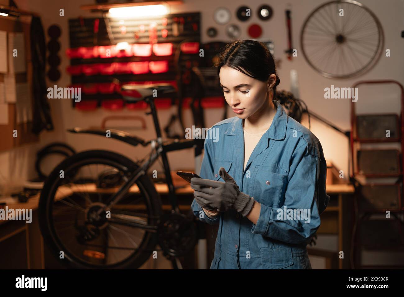Mechanic reading a message on smartphone in bicycle workshop, she is repairing or servicing in a garage Stock Photo
