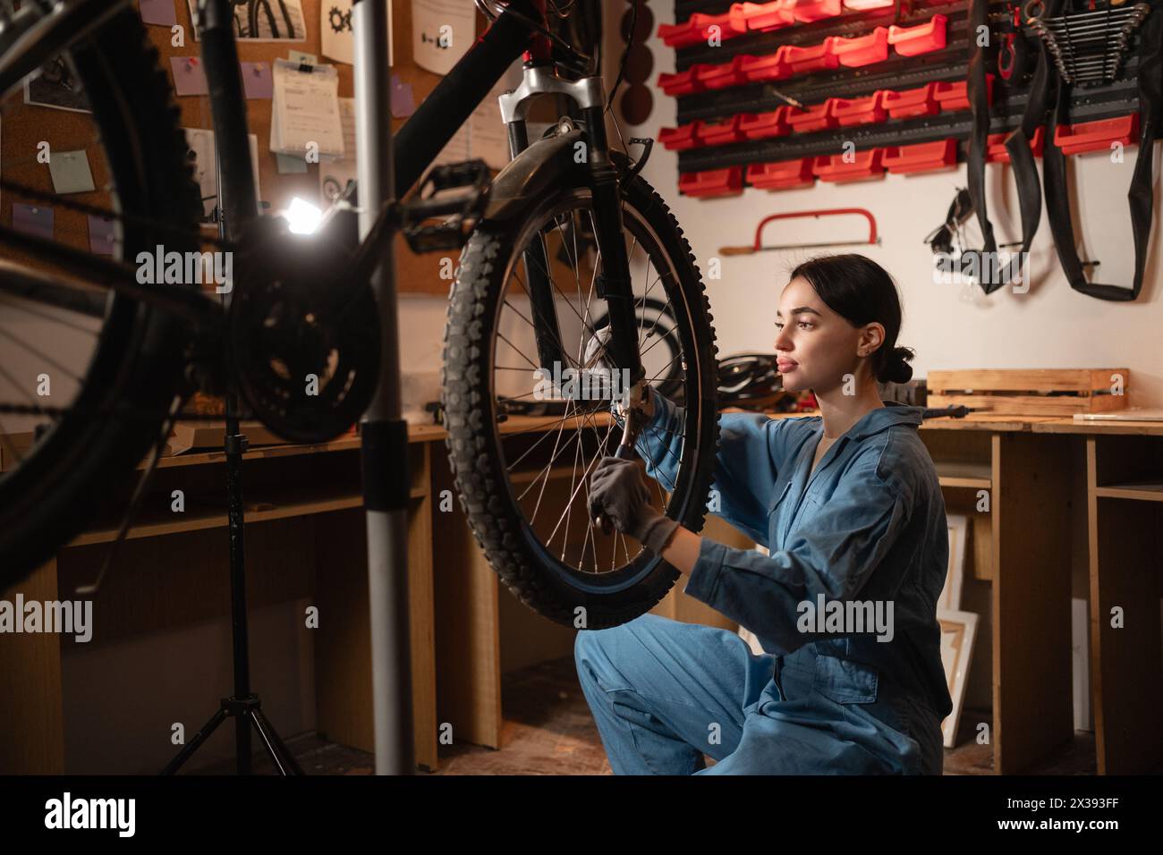 Bicycle female mechanic squatting repairing bike doing his professional work in workshop or garage. Stock Photo