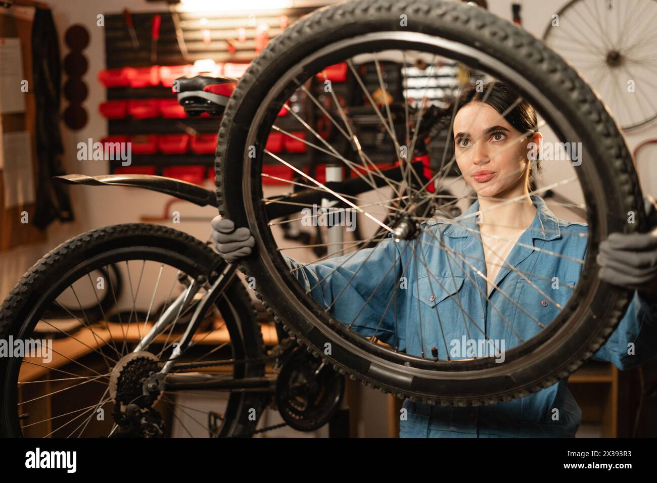 Caucasian young female worker holding and repairing bicycle wheel in bicycle workshop or authentic garage. Stock Photo