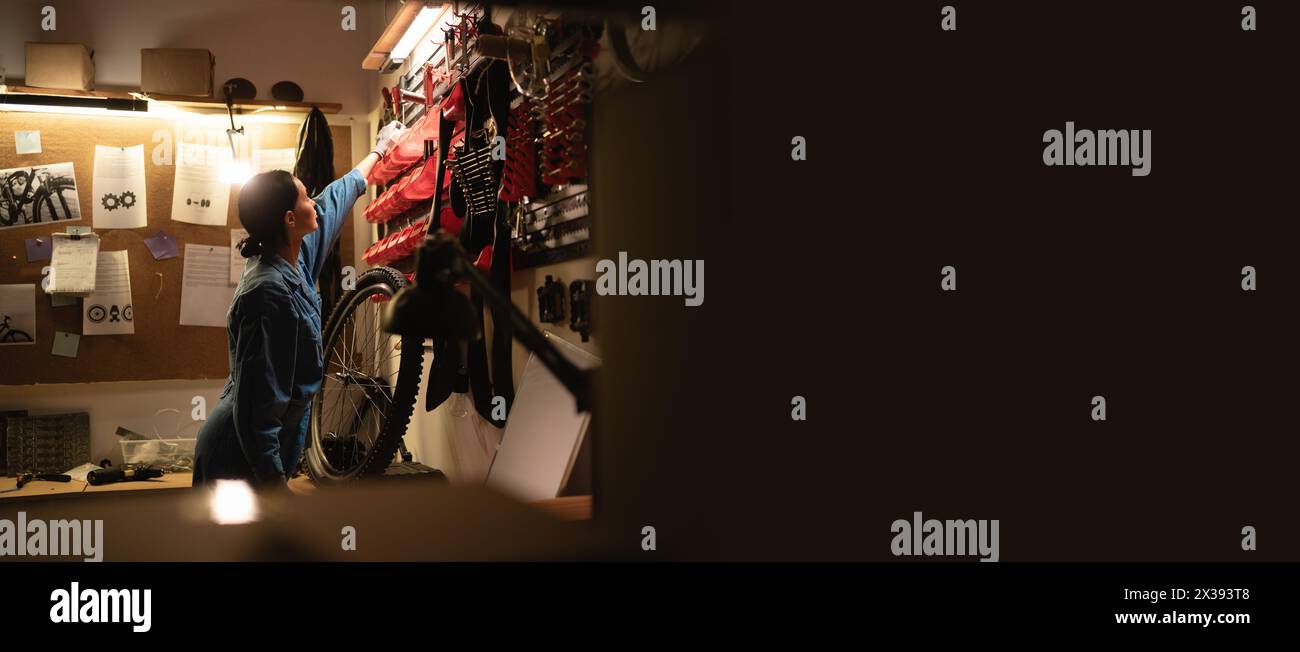 Side view of female mechanic in workshop scene. Tools hanging on wall in garage, Tool shelf against a table and wall, woman working in vintage garage Stock Photo