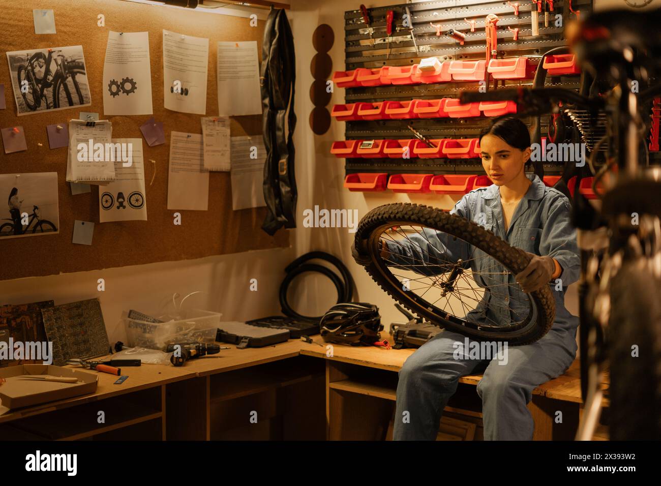 young caucasian female cycling mechanic checking bicycle wheel in workshop or garage. Bike service, repair and upgrade concept. Stock Photo