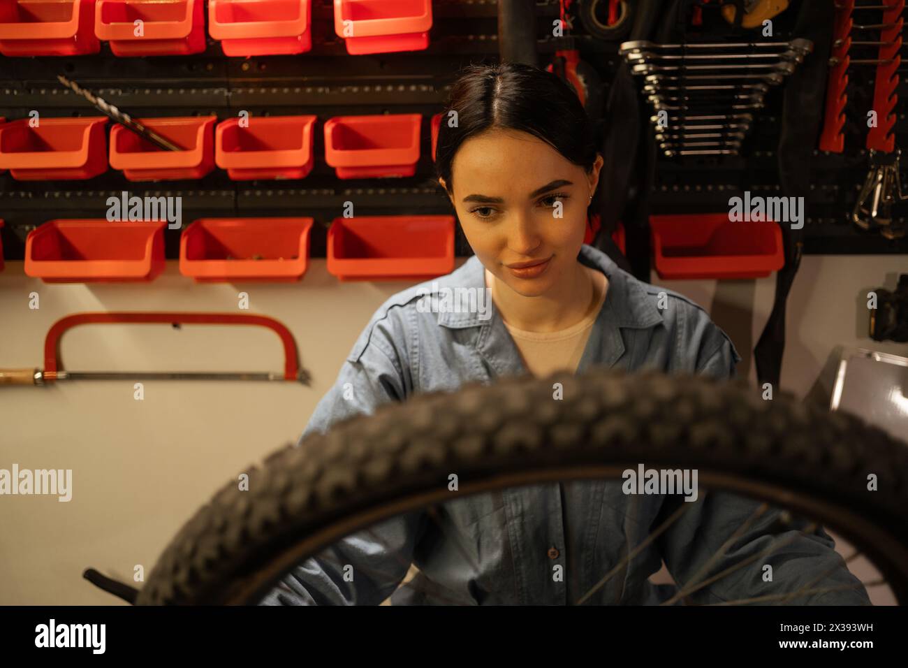 young caucasian female cycling mechanic checking bicycle wheel in workshop or garage. Bike service, repair and upgrade concept Stock Photo