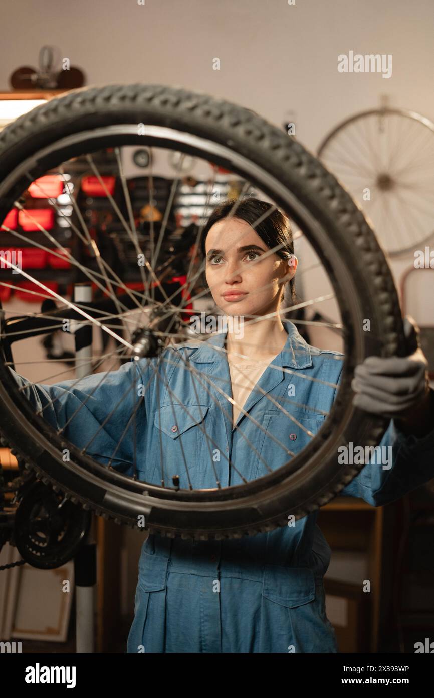 Caucasian young female worker holding and repairing bicycle wheel in bicycle workshop or authentic garage. Stock Photo