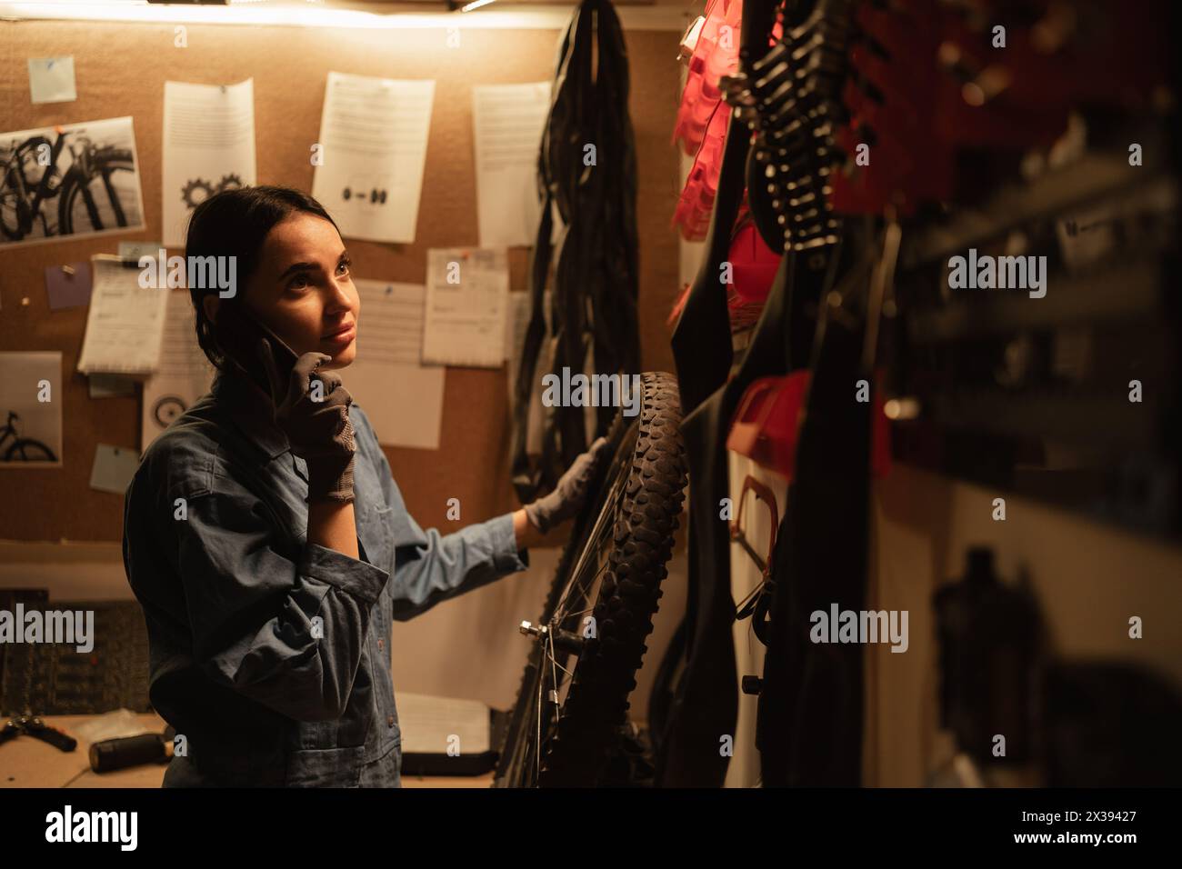 Cute girl mechanic working in a workshop with bicycle wheel talking on a mobile phone Stock Photo