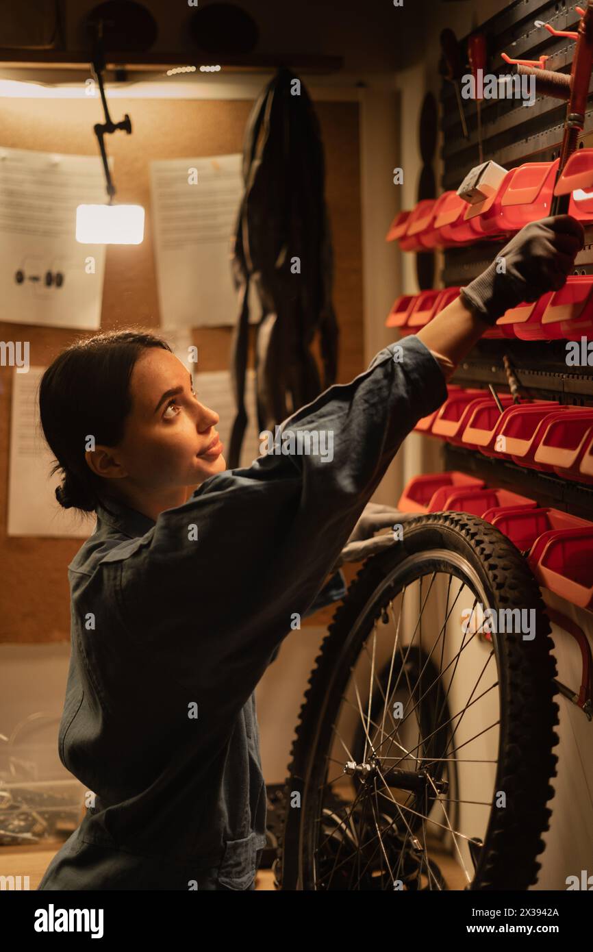 Female mechanic in bike workshop under repair against wall with tools in garage Stock Photo