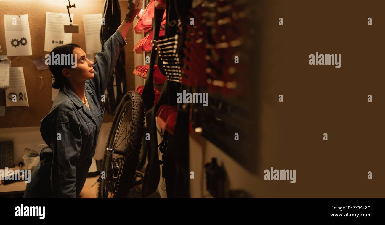 Side view of female Mechanic in a bicycle repair shop looking on wall with tools and equipment Stock Photo