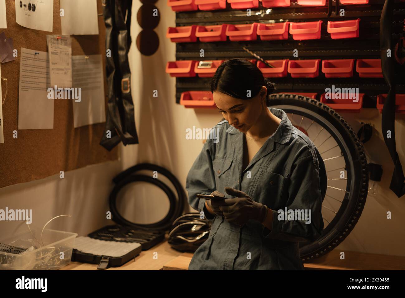 Girl mechanic repairing a bike in a workshop or garage using a smartphone to find the problem of a broken bicycle Stock Photo