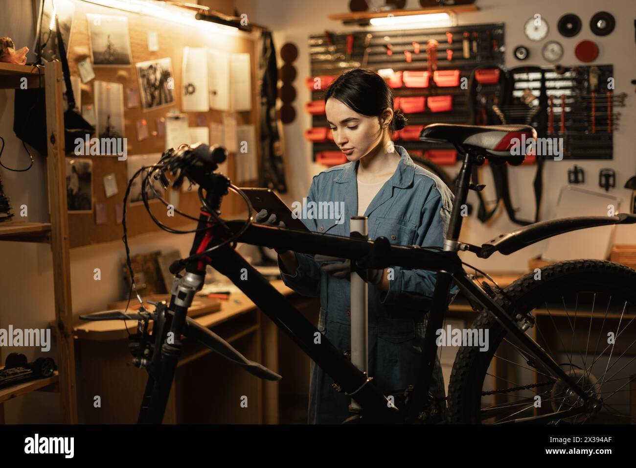 Female mechanic wearing workrobe using digital tablet standing near the bike at the garage or workshop Stock Photo