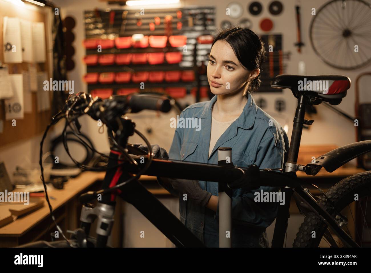 Young female mechanic repairing bike in workshop or garage. Bike workshop interior. Stock Photo