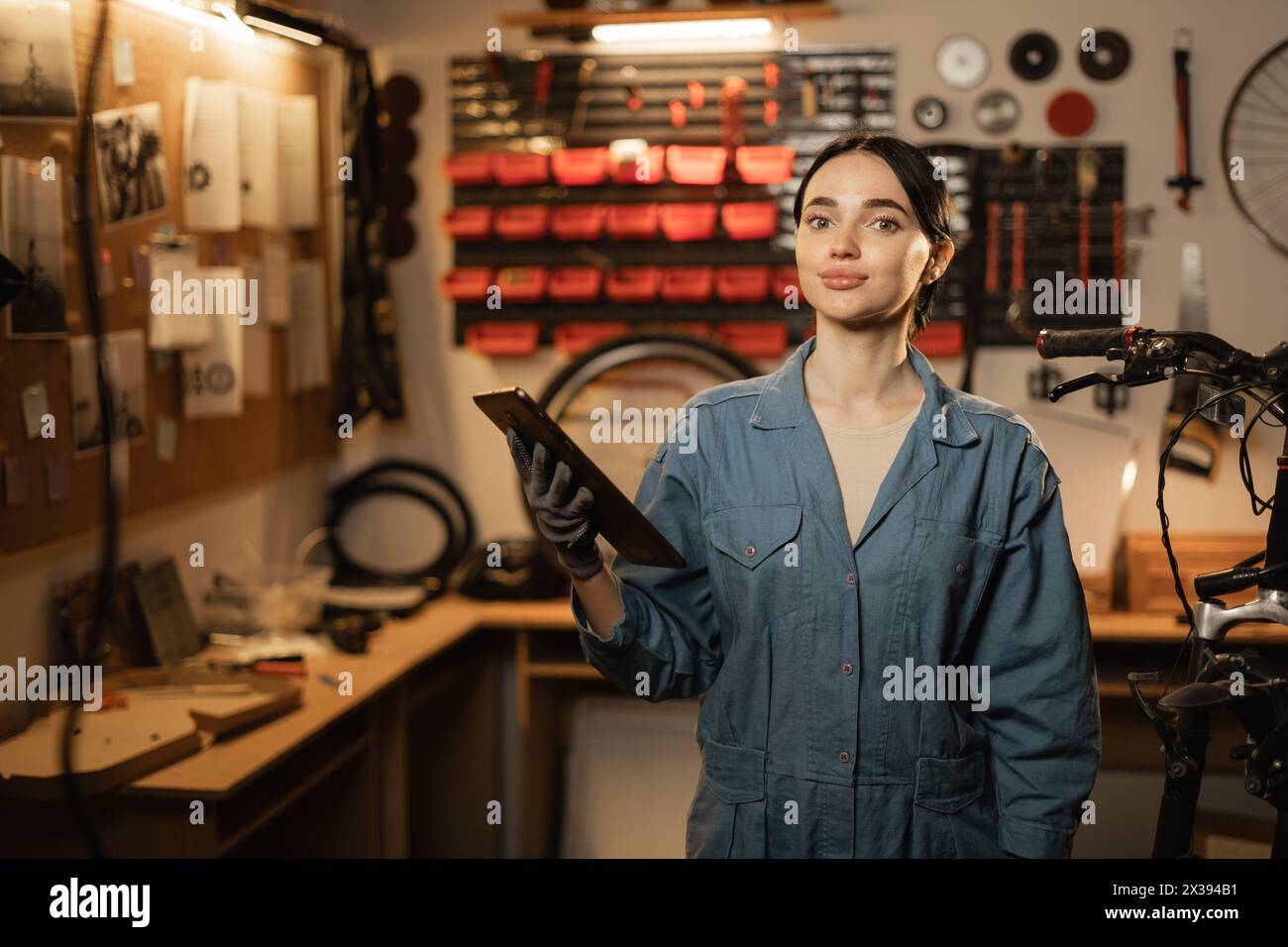 Happy female supervisor mechanic with cheerful smile, inspects repair with tablet at garage, service bike maintenance Stock Photo