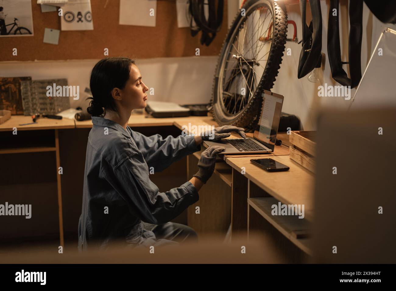 Young beautiful woman in casual clothes using laptop and smiling while working in bike repair shop or garage Stock Photo