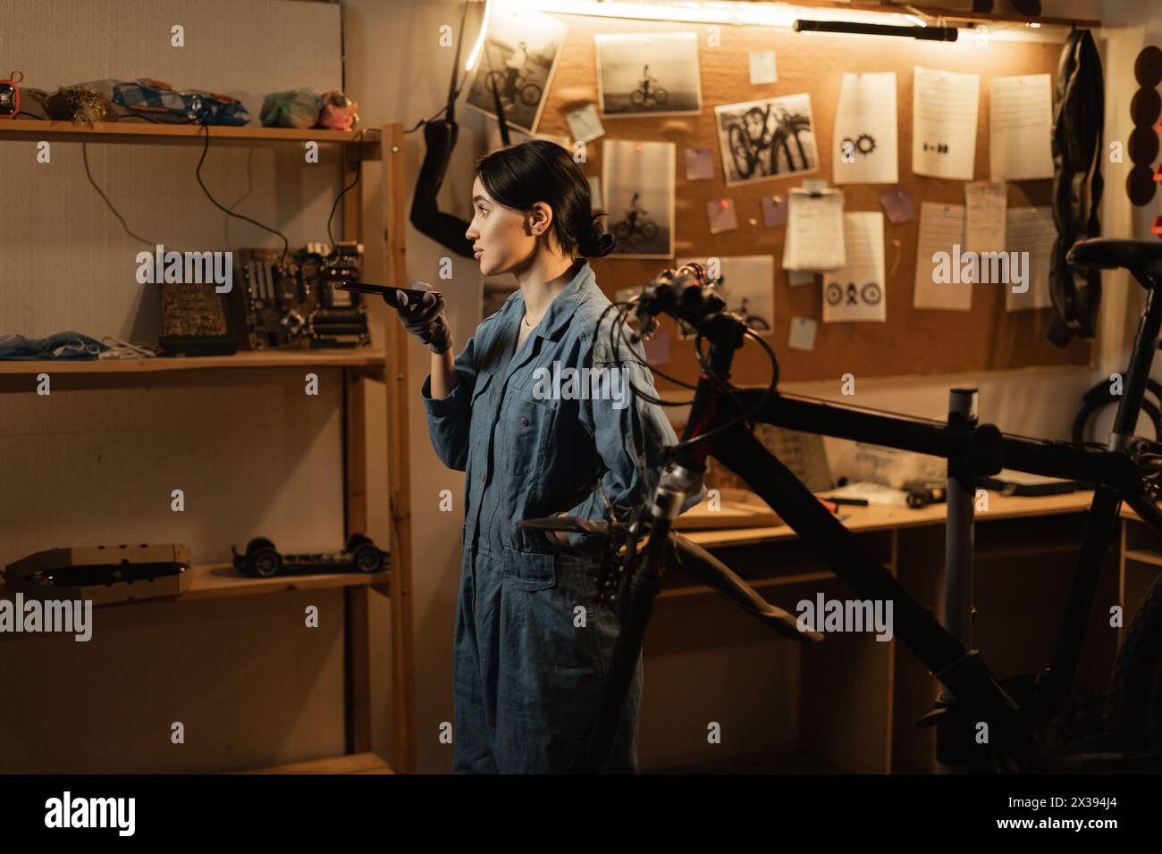 Pretty woman repairing bike in garage, holding in hand smartphone talking with digital assistant uses voice messaging, voice recognition Stock Photo