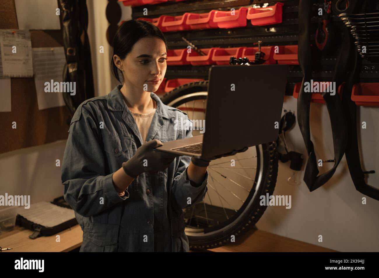 Young female mechanic in bike workshop working and researches information on his laptop Stock Photo