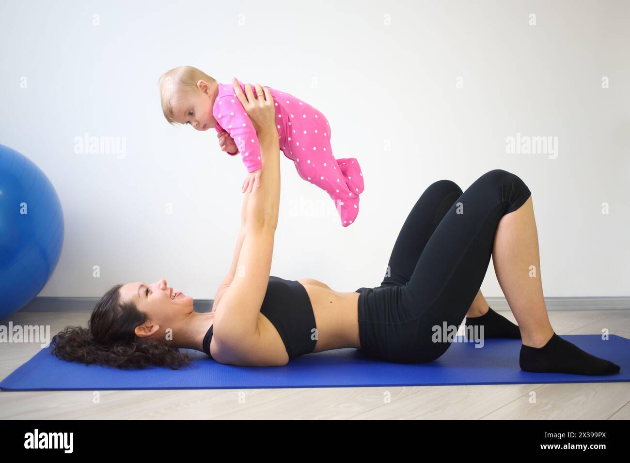 Happy woman lying on her back on the floor lifted up baby in the gym Stock Photo