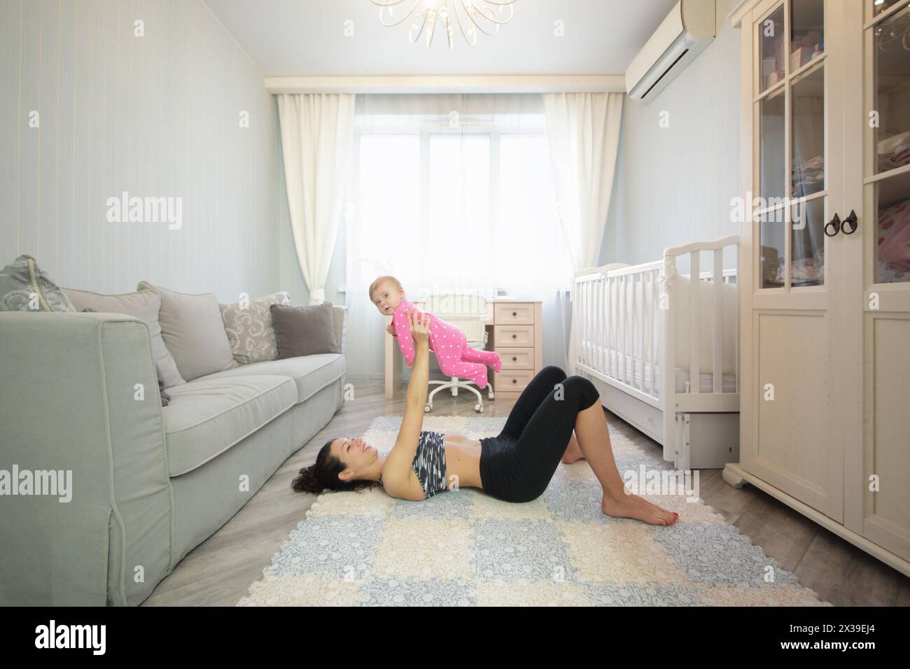 Happy woman lying on the floor on her back lifted up baby in the room Stock Photo