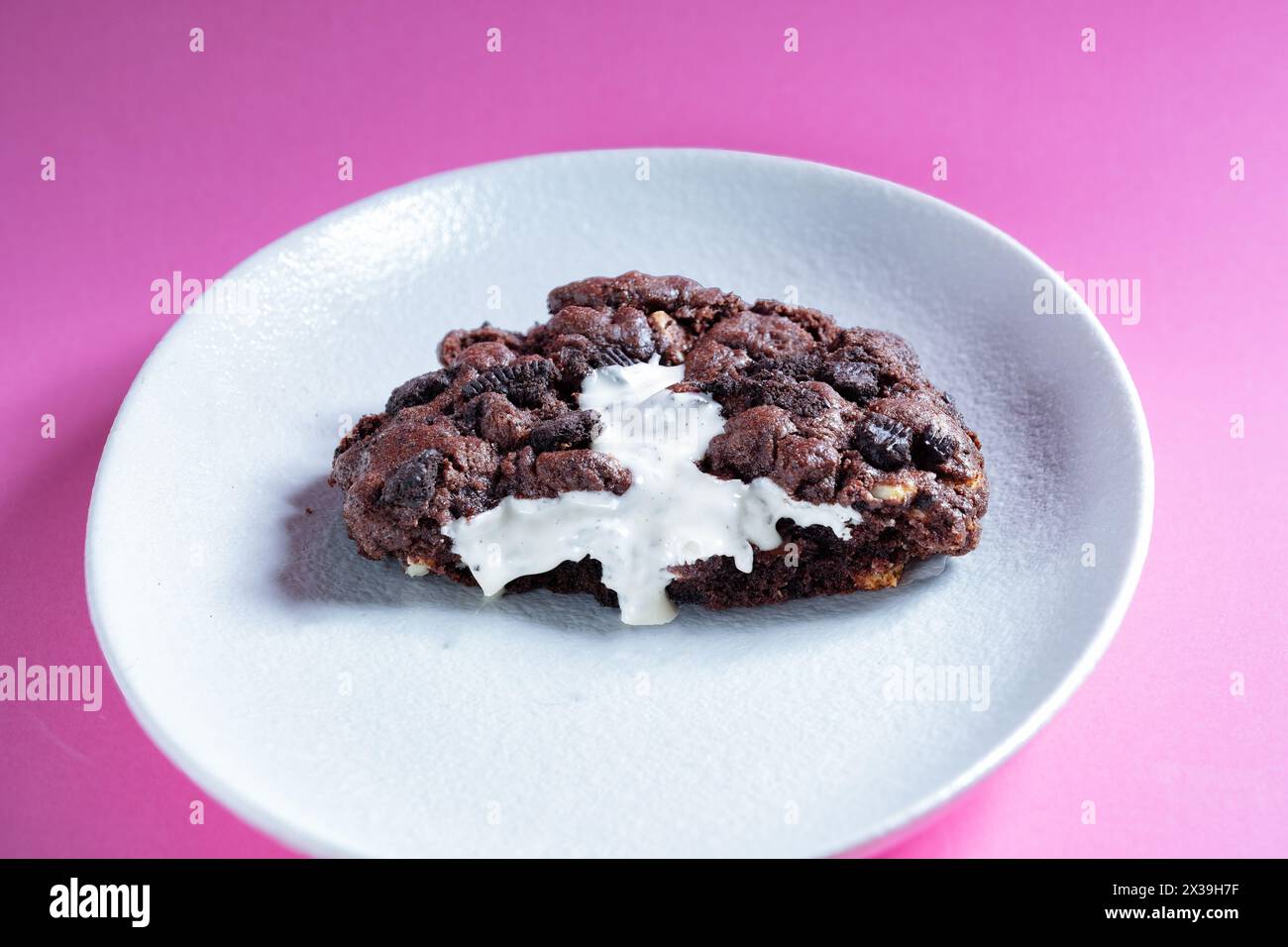 A large freshly made warm NY style Oreo Cookie halved and served on a plate. The cookie is oozing a white chocolate cream filling Stock Photo