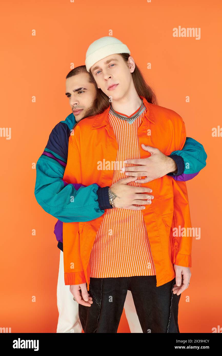 A loving gay couple stands side by side against a bold orange backdrop. Stock Photo