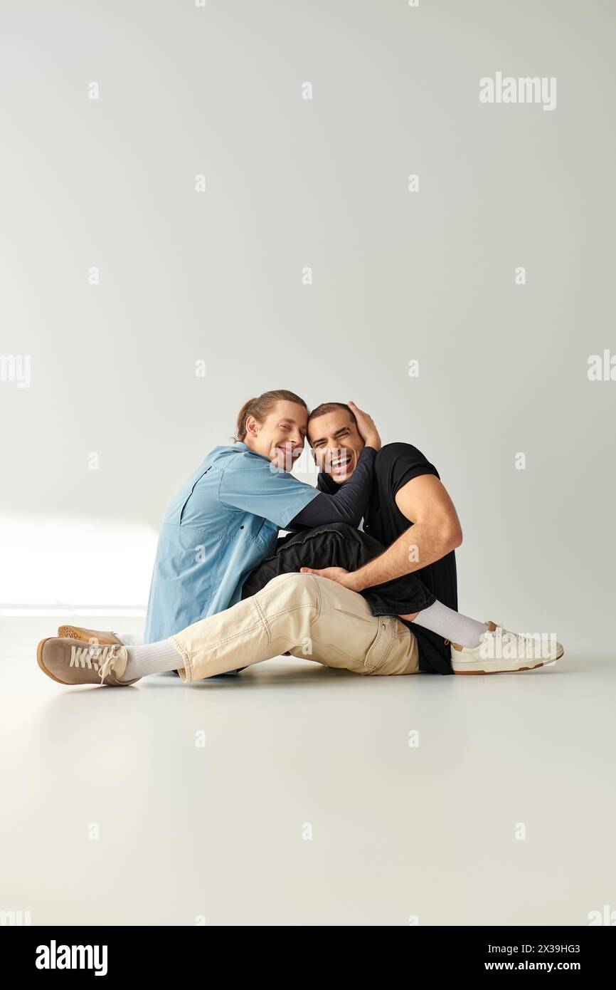 Two men, an appealing and loving gay couple, sitting gracefully on a white floor. Stock Photo