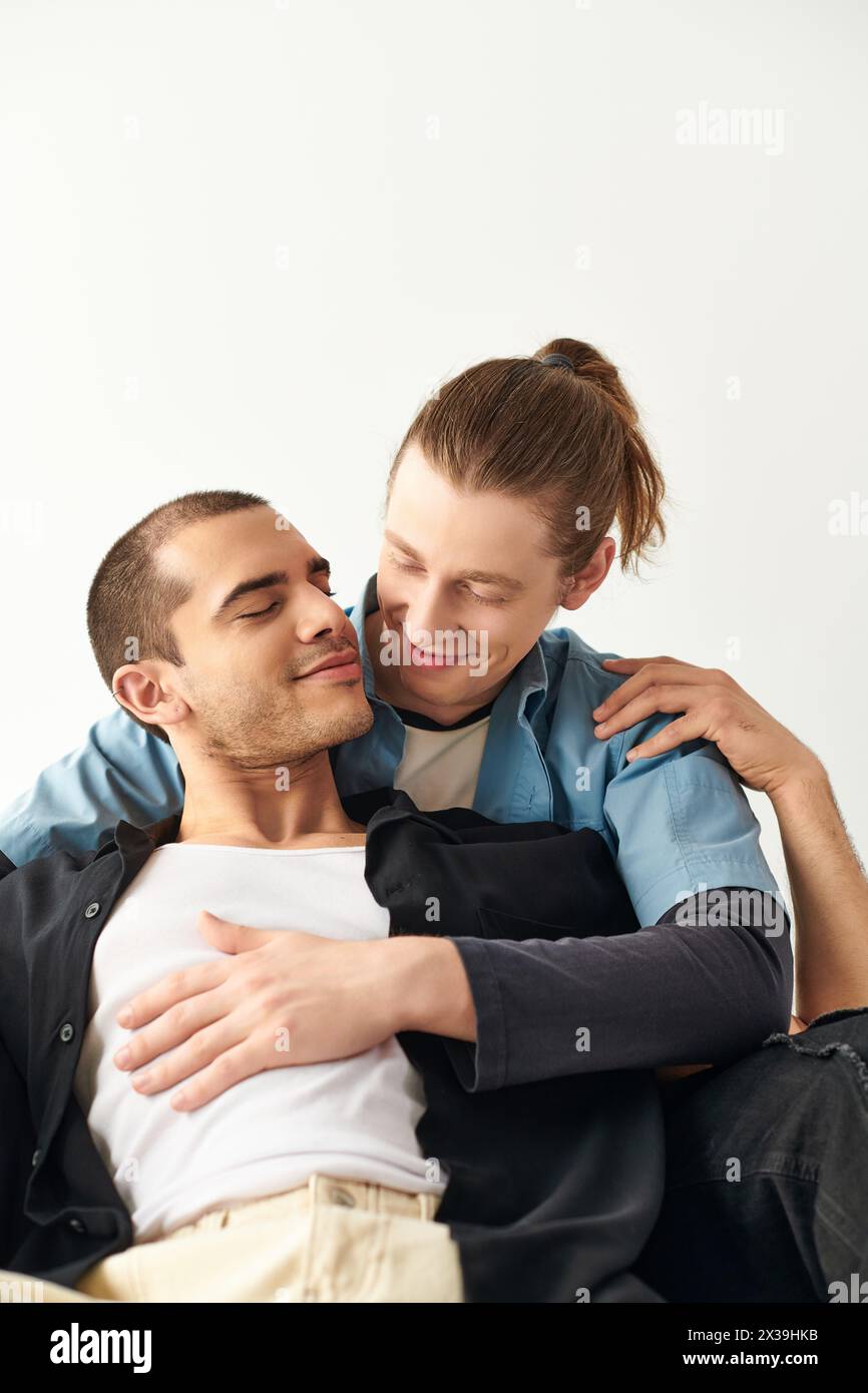A man sits on top of another man on a couch in a loving and intimate moment. Stock Photo