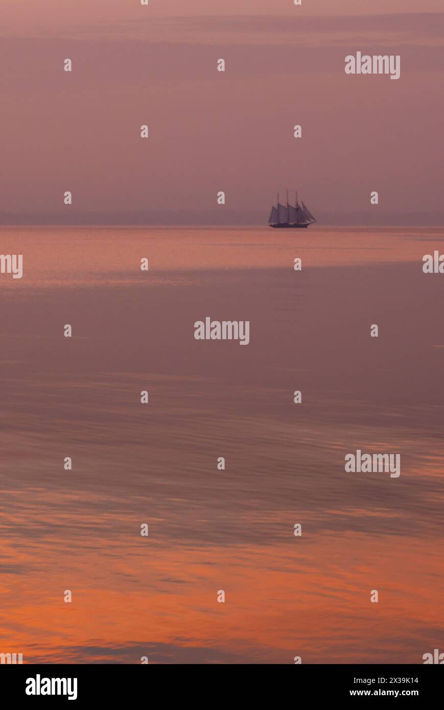 A lonely full rigged ship passing in peach morning light Stock Photo