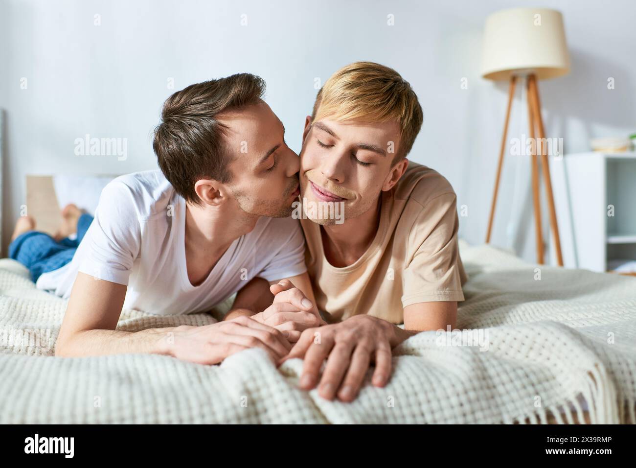 Two men laying on a bed, sharing a passionate kiss. Stock Photo