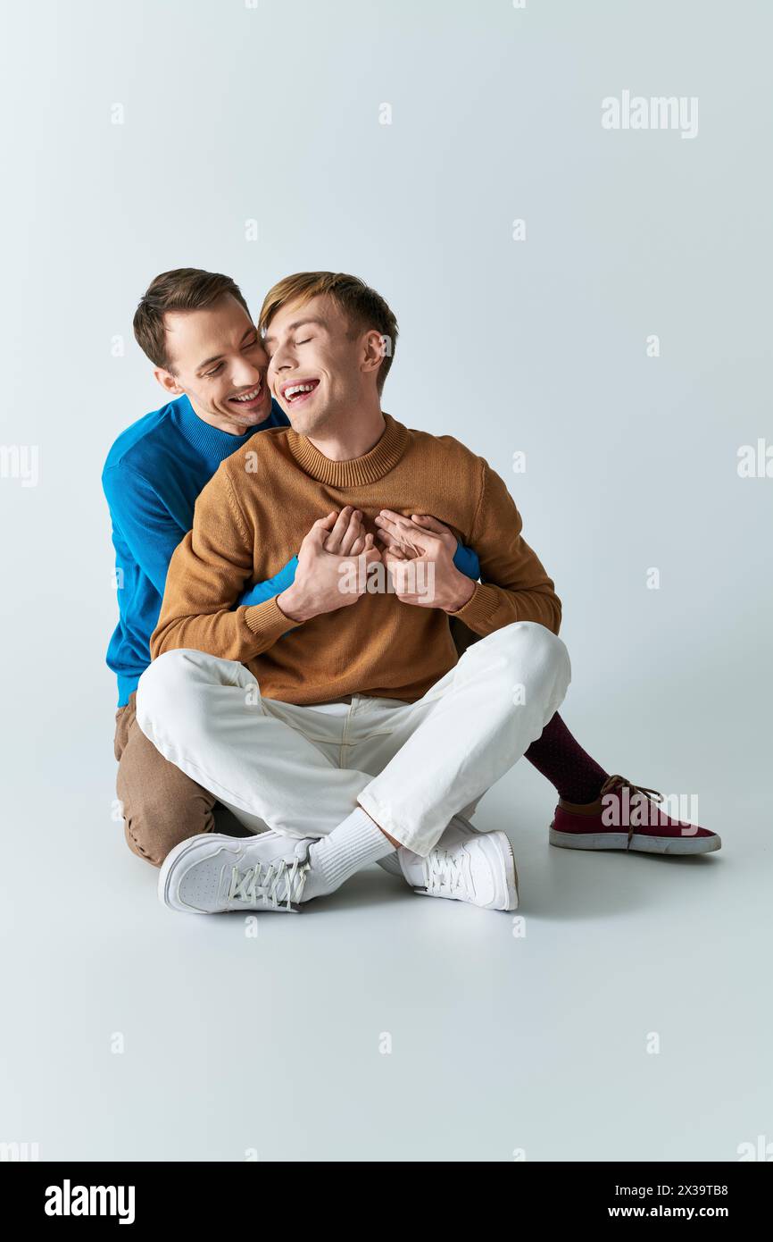 Two men wearing casual attire, sitting on the ground, sharing a hug. Stock Photo