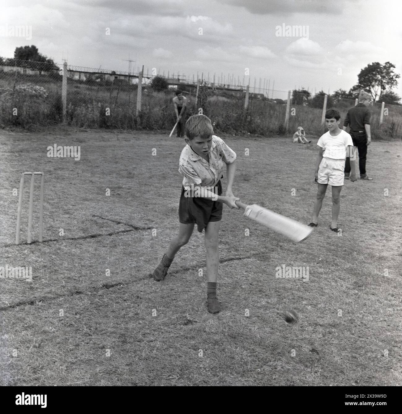 1960s, historical, outside in a field, a young boy playing cricket, concentration and effort, as infront of the stumps, he puts bat onto ball, England, UK. Stock Photo