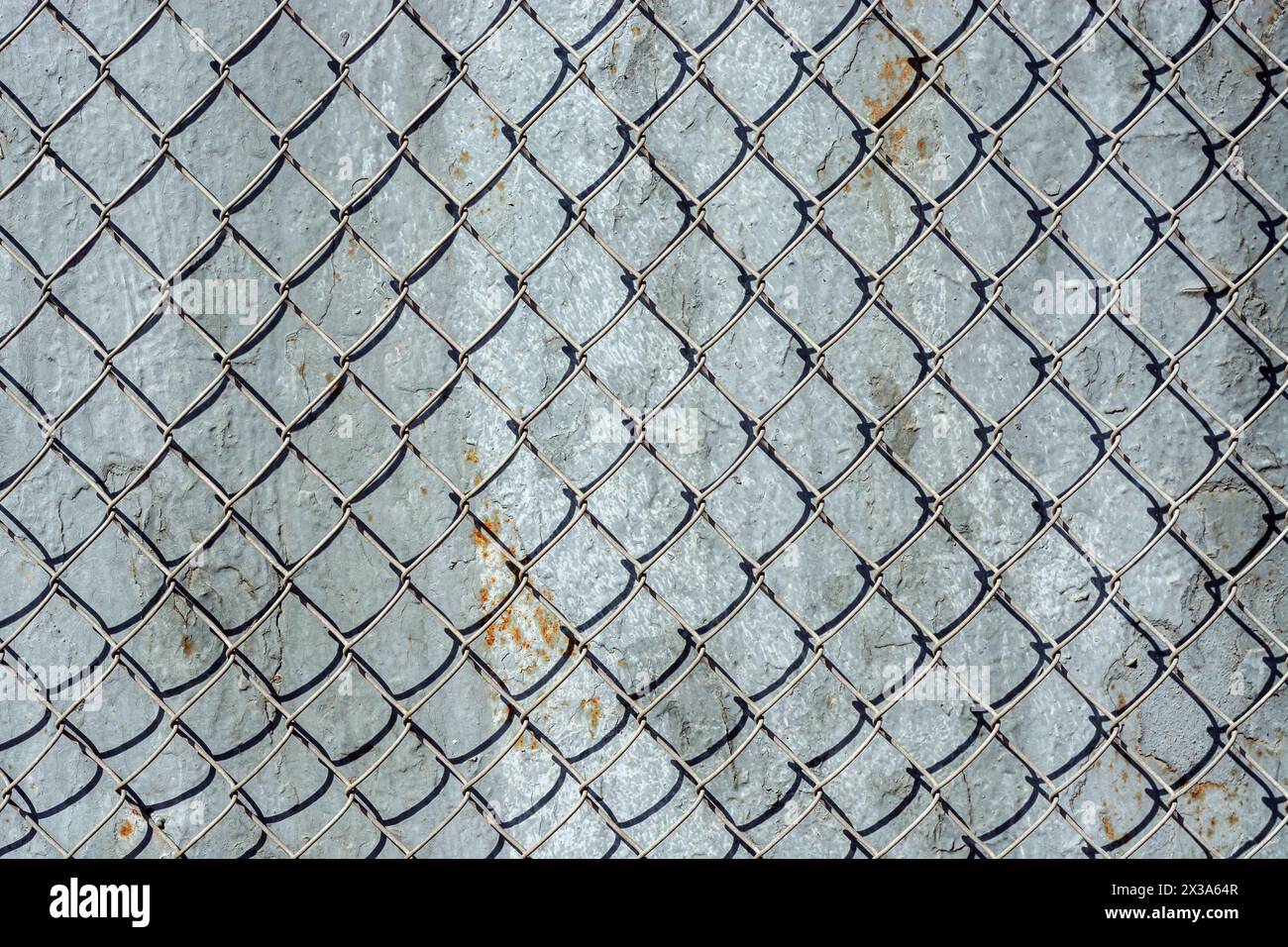 Fragment of an iron mesh with square cells against the background of a wall covered with peeling gray paint with rust, for use as an abstract backgrou Stock Photo