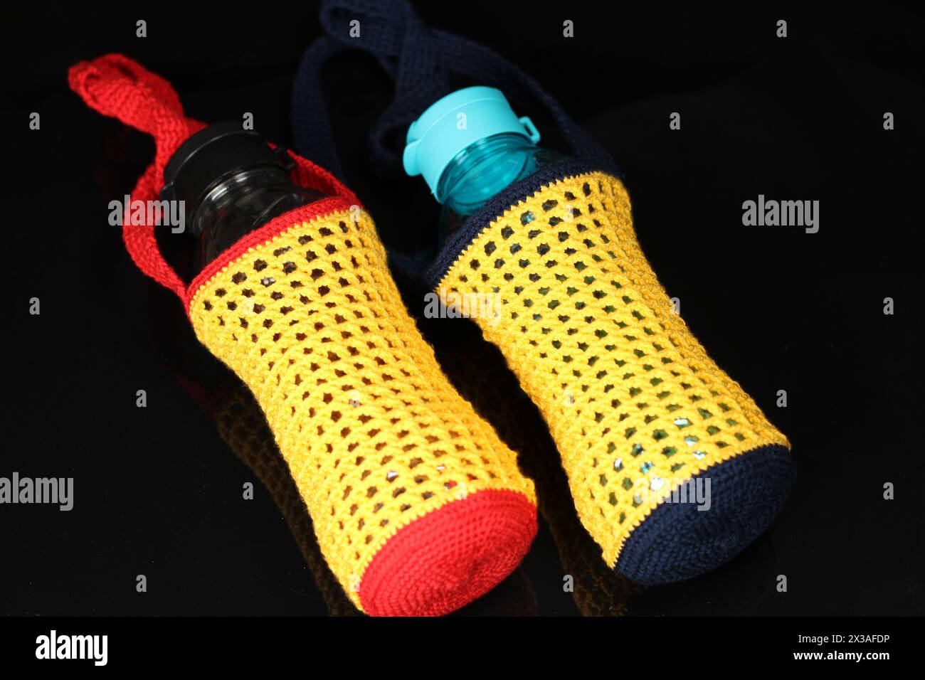 Knitted red, yellow and blue drinking water bottle holder isolated on black background. Stock Photo